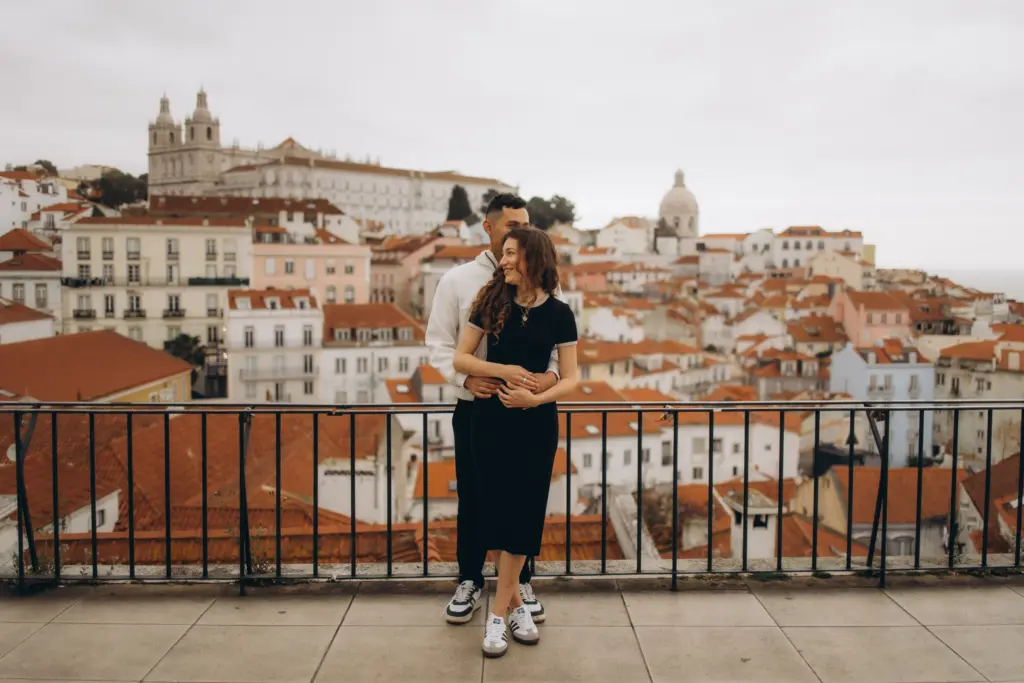 Couple at an Alfama viewpoint with the rooftops of Lisbon behind them