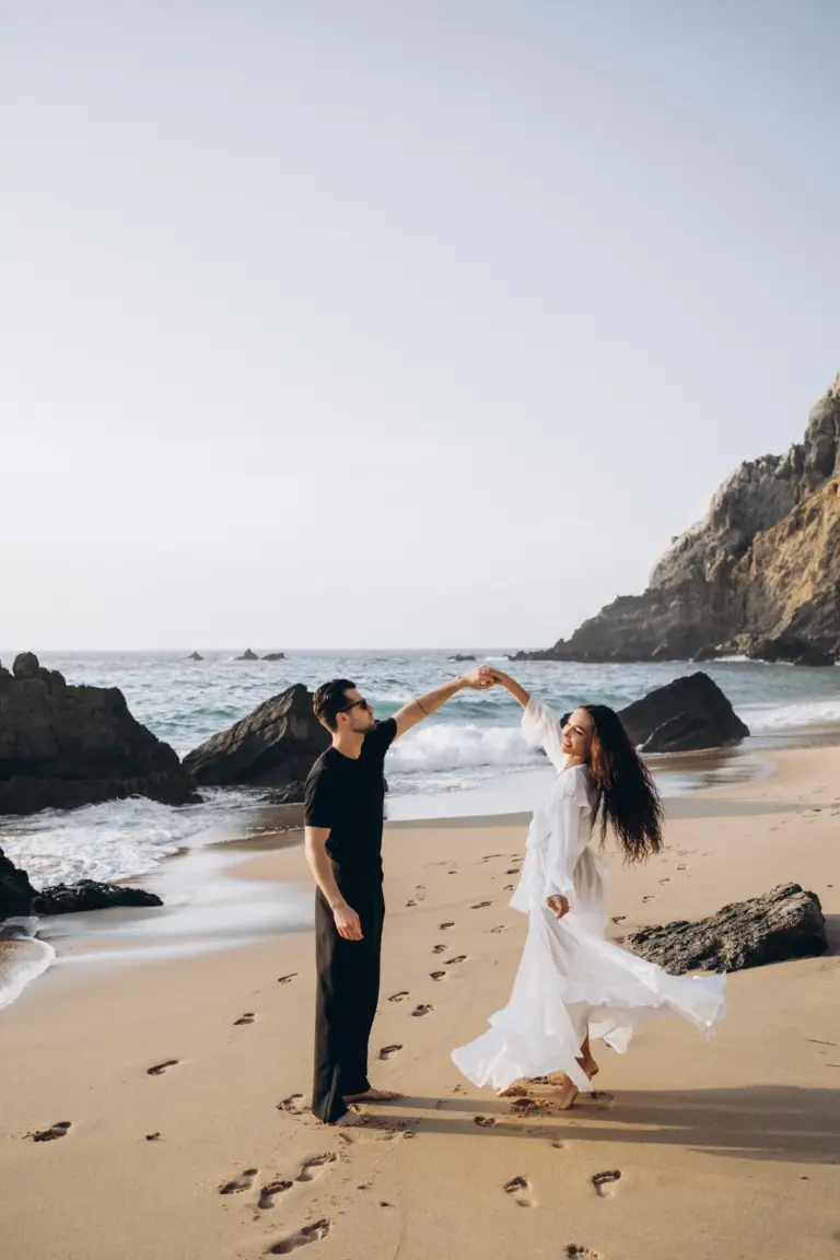 Couple dancing on the beach at Praia da Adraga, her dress in the wind