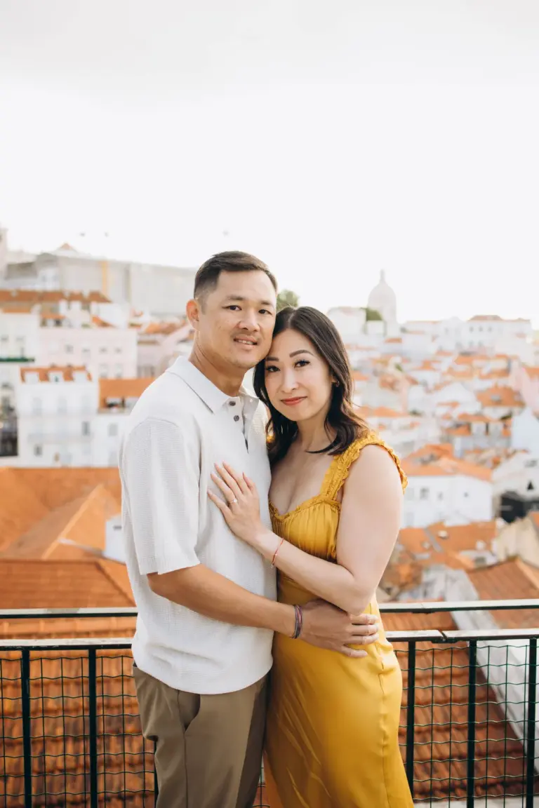 Couple embracing at Miradouro das Portas do Sol, the rooftops of Alfama behind them