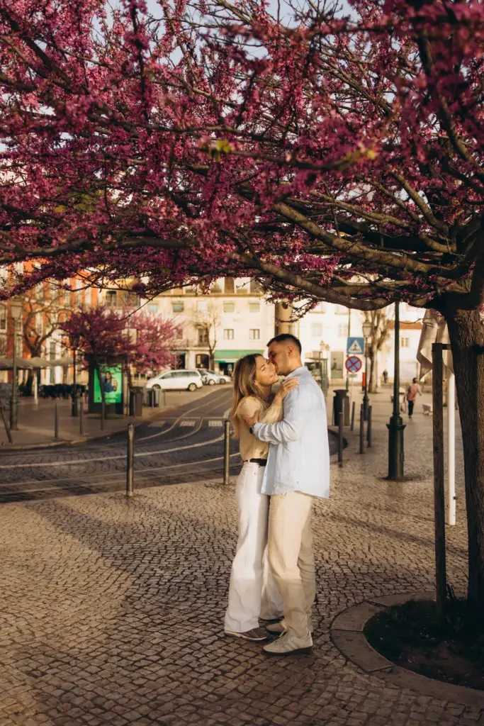 Couple embracing under pink blossom trees on a Lisbon square
