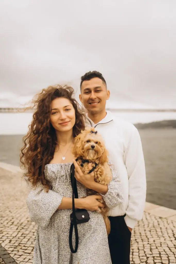 Couple holding their dog by the river, the 25 de Abril Bridge behind them
