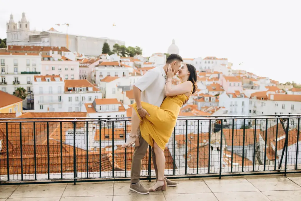 Man lifting his partner at an Alfama viewpoint, São Vicente church behind them