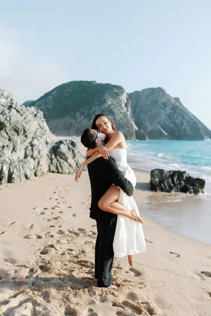 Man lifting his partner on the sand at Praia da Adraga