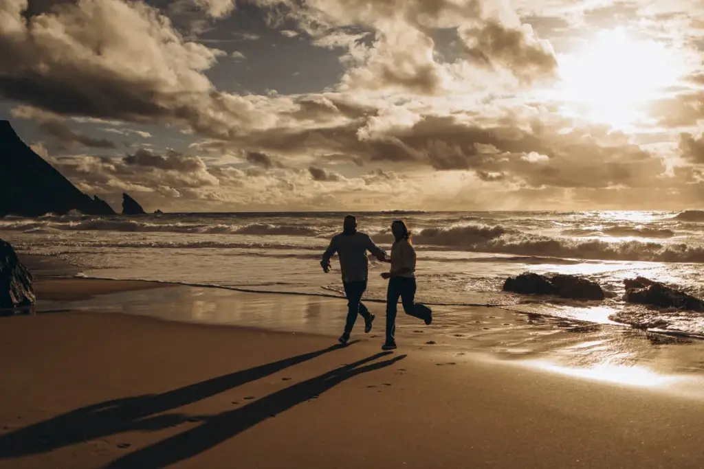 Couple running along the beach at Praia da Adraga under a dramatic sky