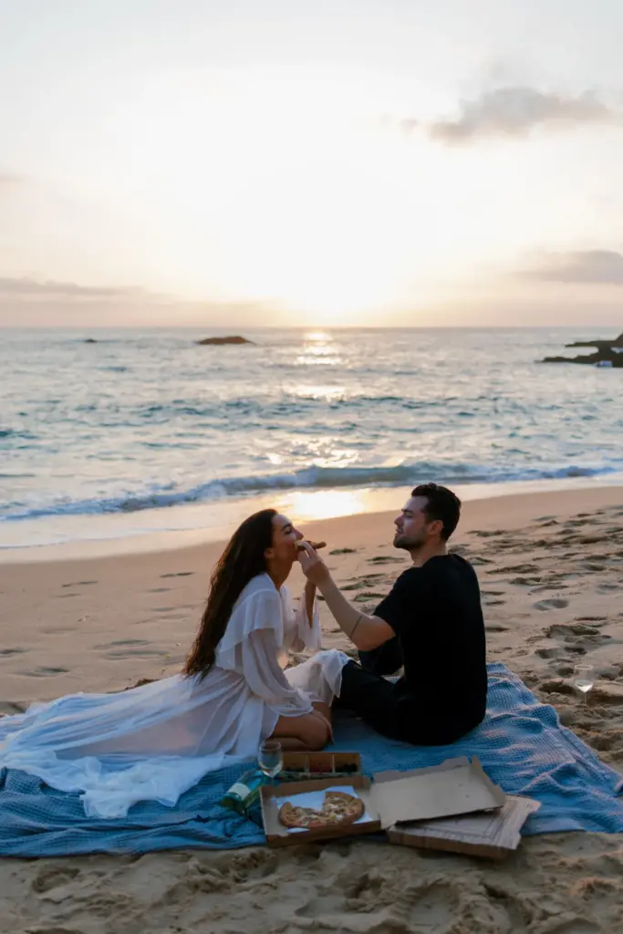 Couple sitting on the beach at Praia da Adraga as the sun sets