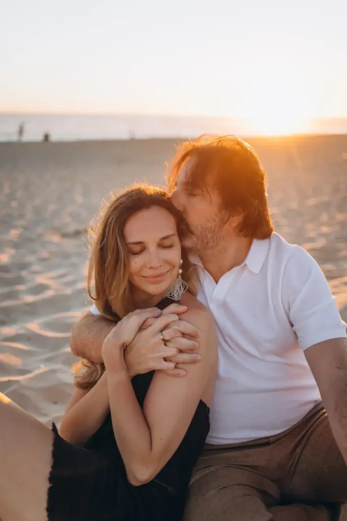 Couple sitting close on the sand, the ocean behind them