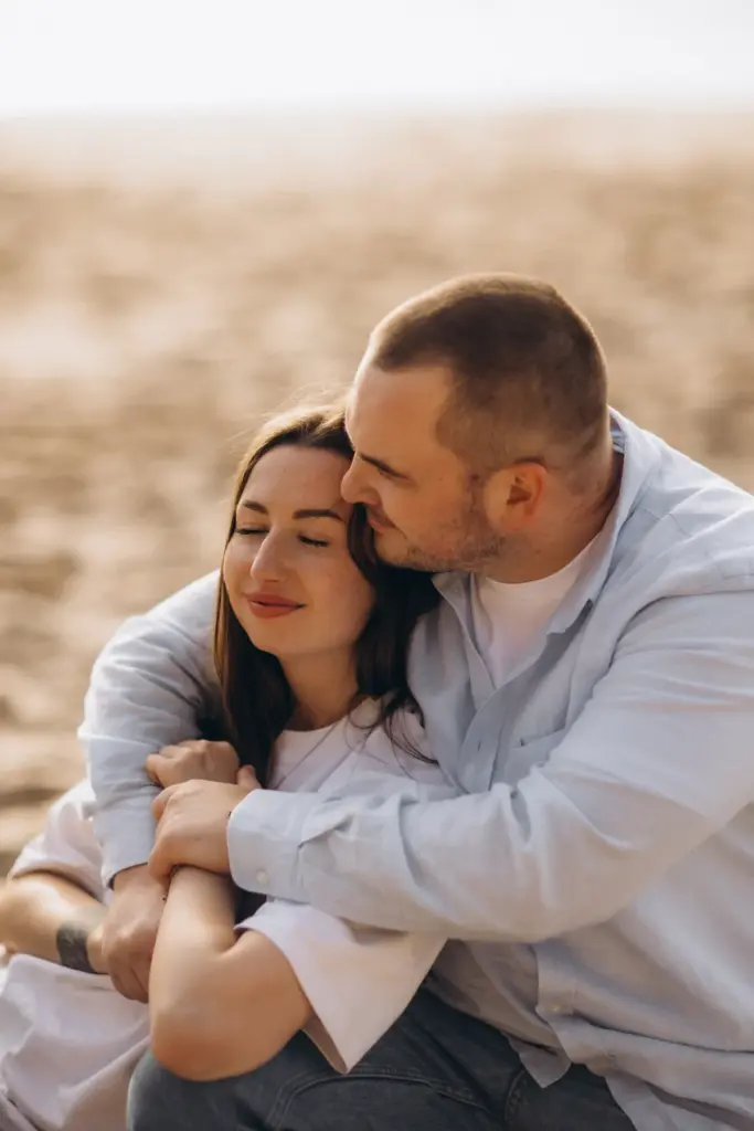 Couple sitting close together on the beach at Praia da Adraga