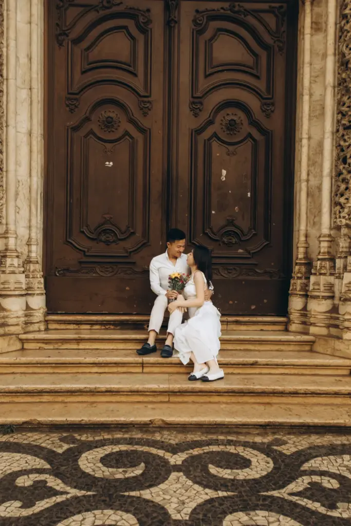 Couple sitting on the steps of a carved wooden church door in Lisbon