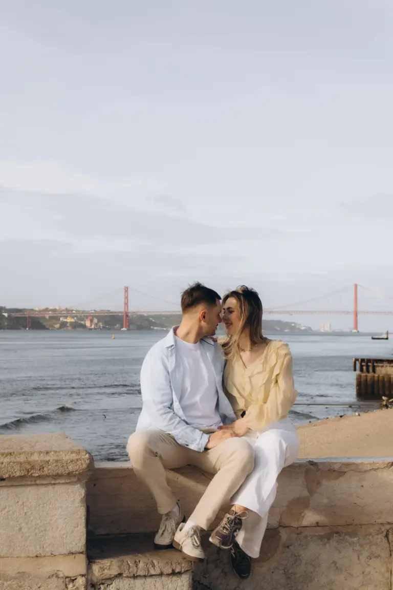 Couple sitting on the Tagus riverfront with the 25 de Abril Bridge behind