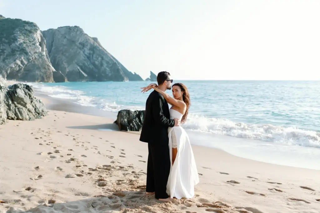 Couple standing on Praia da Adraga with the sea stacks behind them