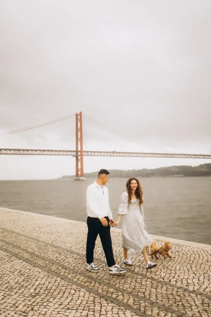 Couple walking their dog by the river, the 25 de Abril Bridge behind them