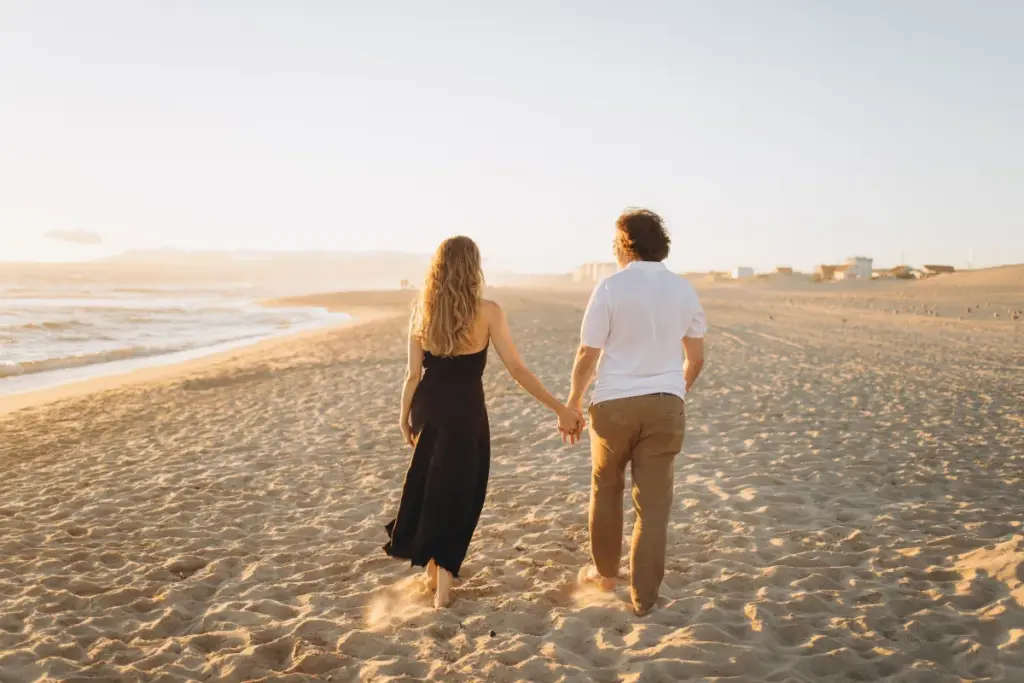 Couple walking hand in hand on the wide beach of Costa da Caparica