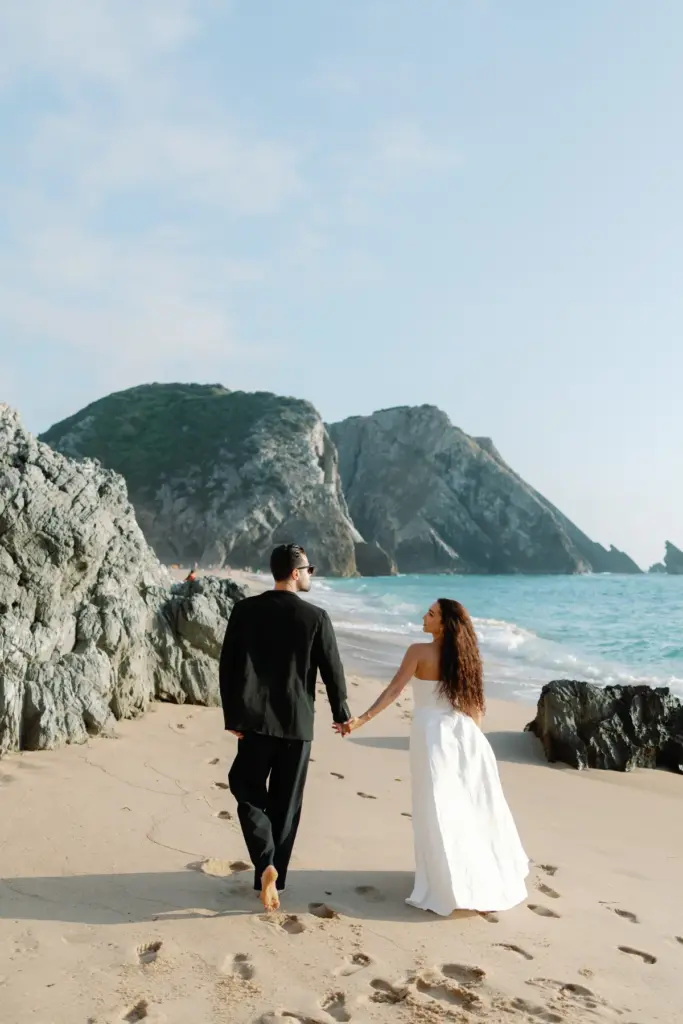 Couple walking hand in hand towards the rocks on Praia da Adraga