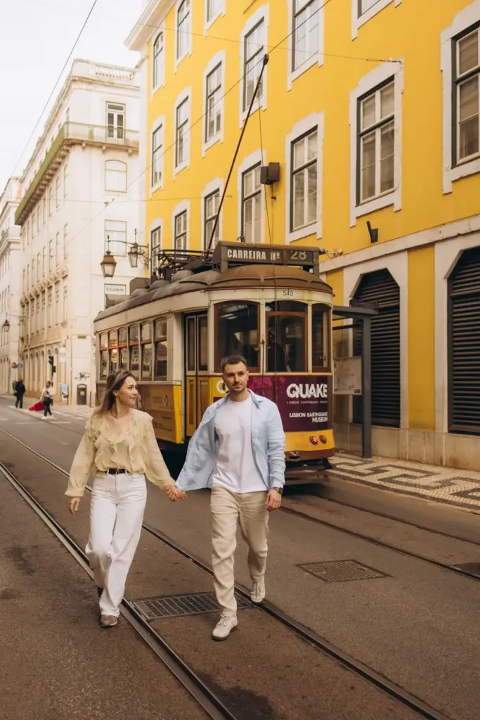 Couple walking hand in hand beside a yellow tram in Baixa