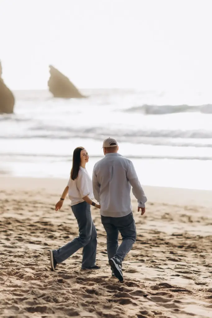Couple walking on Praia da Adraga, the sea stacks behind them