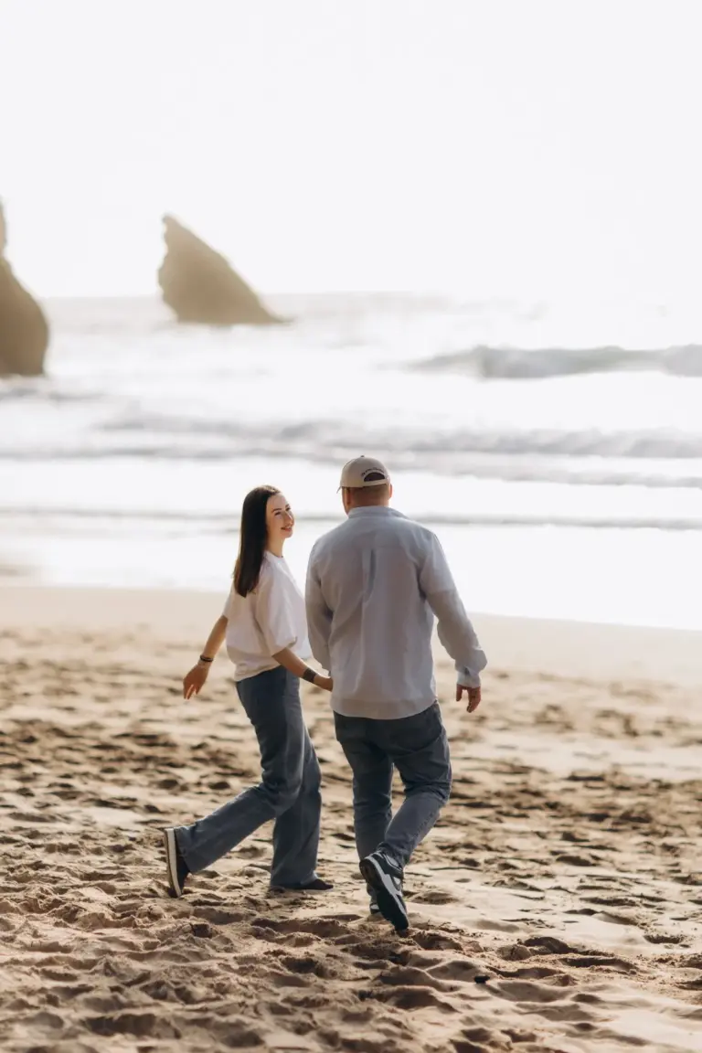 Couple walking on Praia da Adraga, the sea stacks behind them