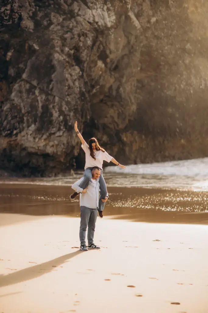 Woman on her partner's shoulders below the cliffs of Praia da Adraga