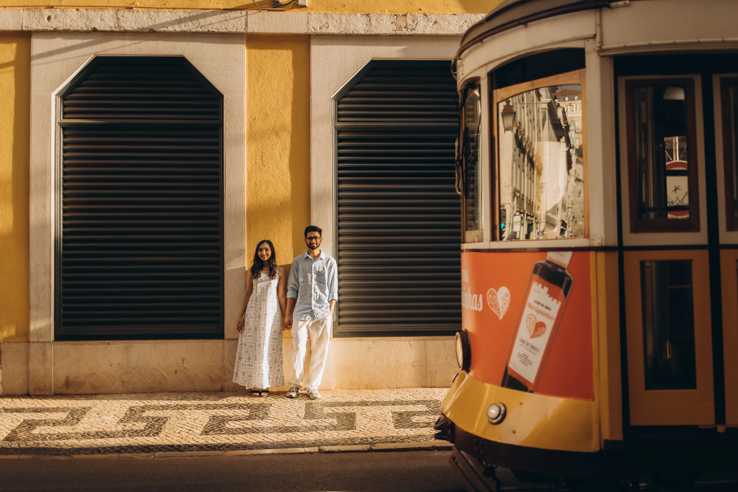 Couple by a yellow tram and a yellow façade in Baixa, Lisbon