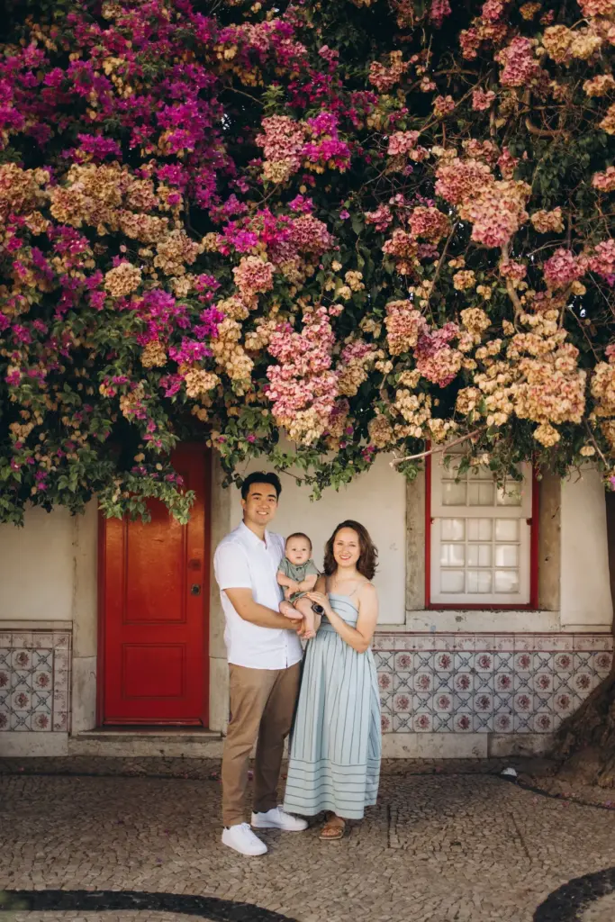 Family with a baby by a red door under bougainvillea in Alfama