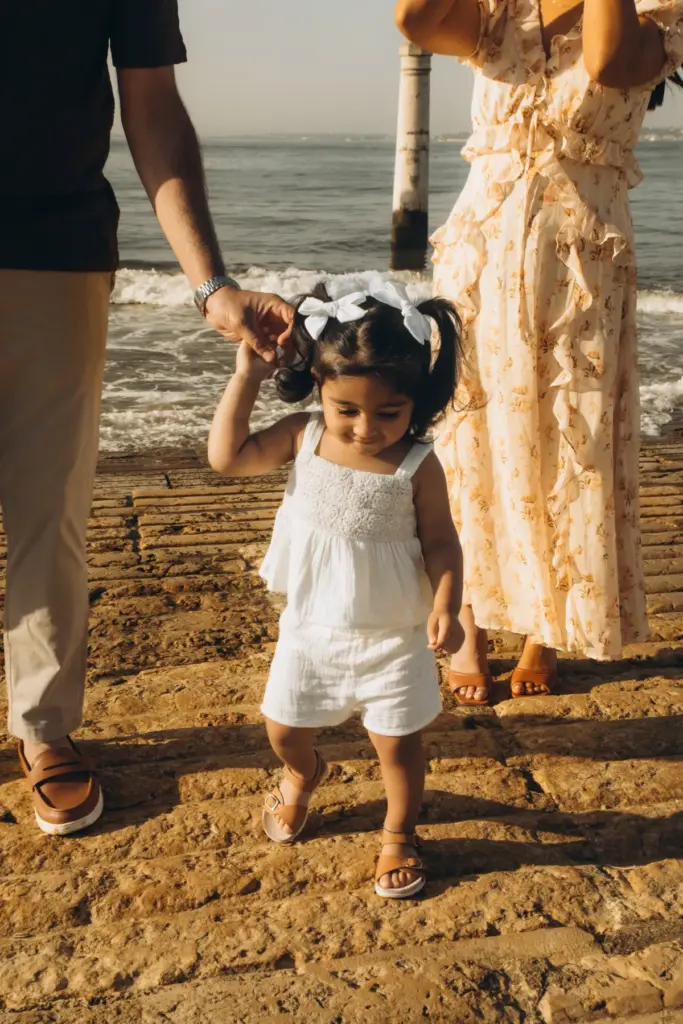 Toddler taking steps between her parents by the Tagus at Cais das Colunas