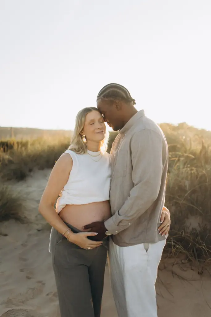 Expecting couple embracing among the grassy dunes