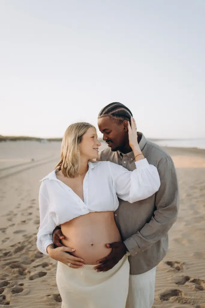 Expecting couple embracing on the sand, hands on the bump