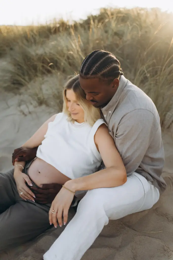 Expecting couple sitting together in the dunes