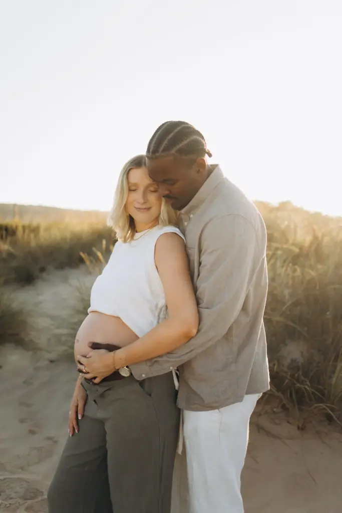 Father-to-be holding his partner's bump in the dunes