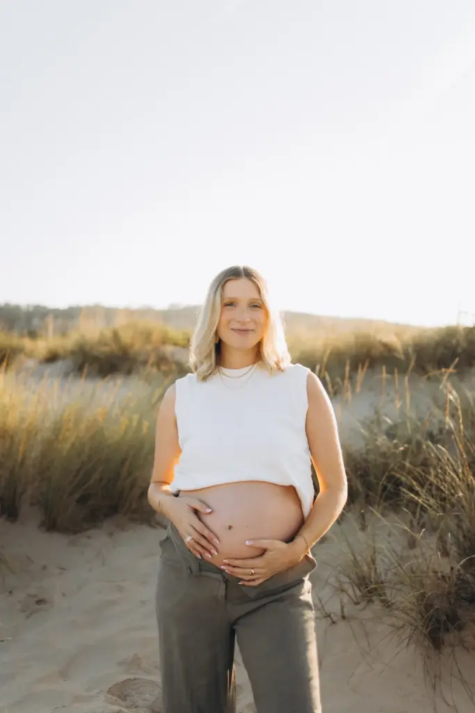 Pregnant woman holding her bump among the dune grass