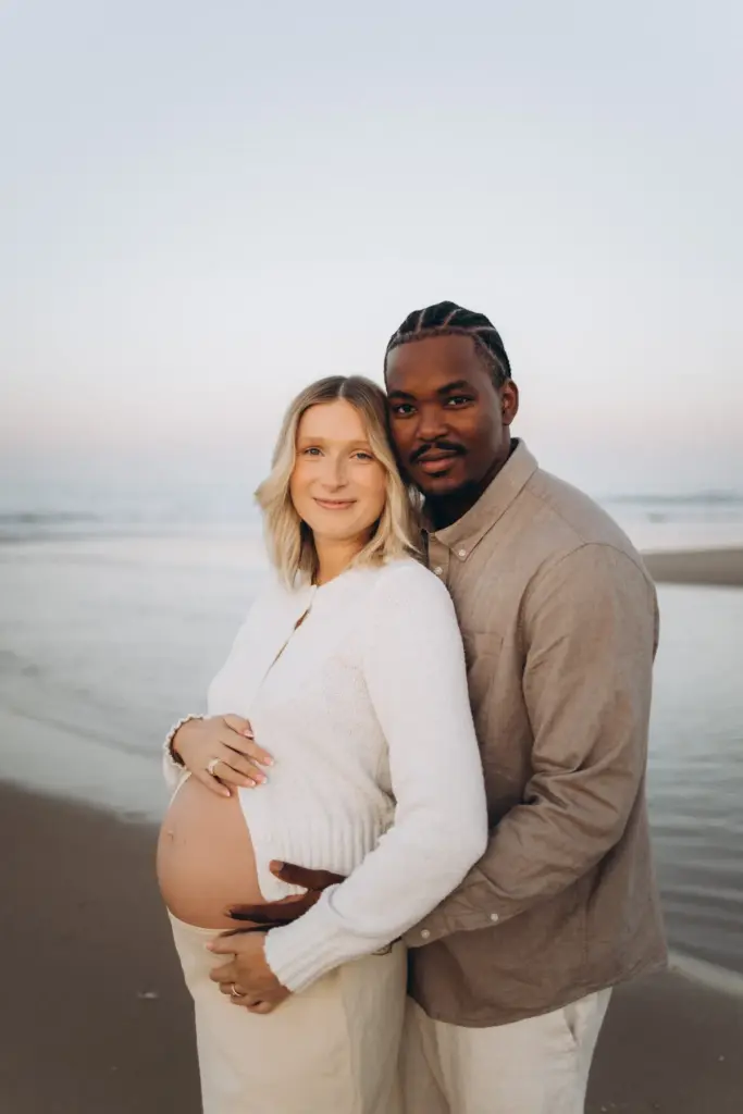 Pregnant woman and her partner on the beach, his hands on her bump