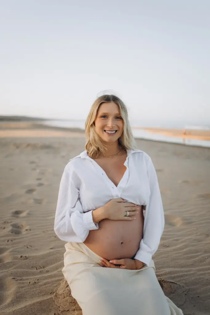 Pregnant woman sitting on the sand holding her bump