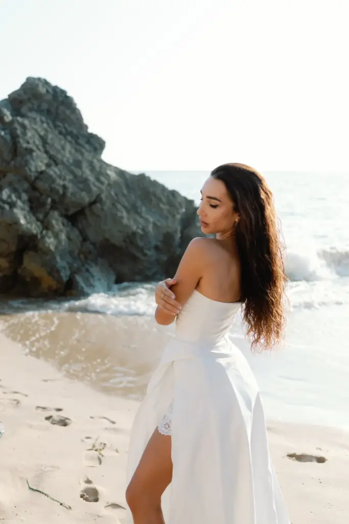 Woman in a white dress by the rocks at Praia da Adraga