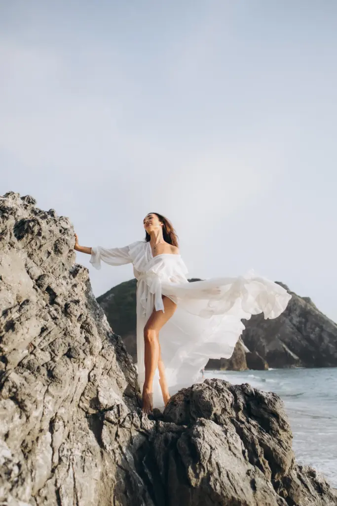 Woman in a white dress on the rocks at Praia da Adraga, the dress in the wind