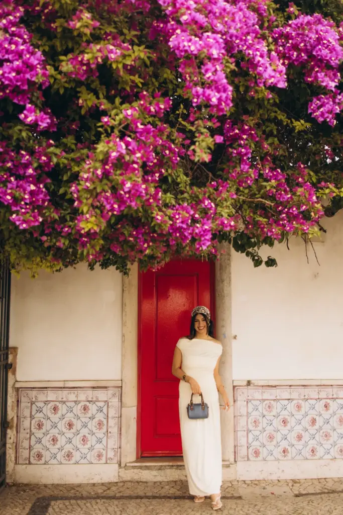 Woman by a red door under bougainvillea