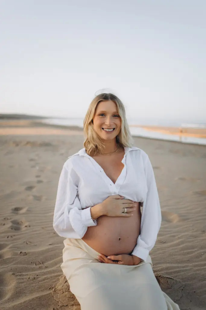 Mum-to-be smiling on the beach in soft evening light