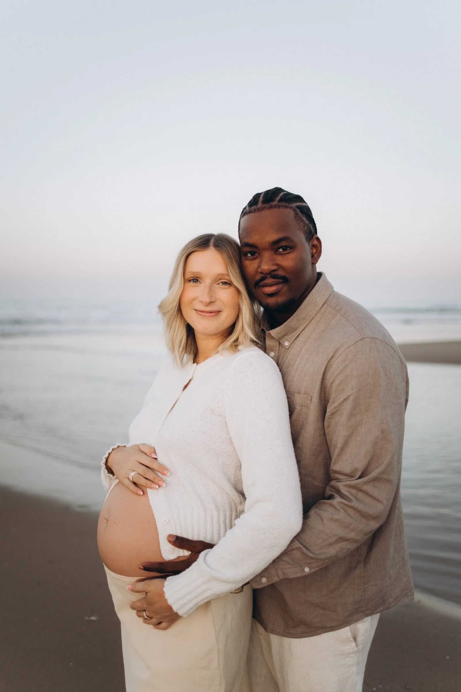 Pregnant woman and her partner on an Atlantic beach near Lisbon, his hands on her bump