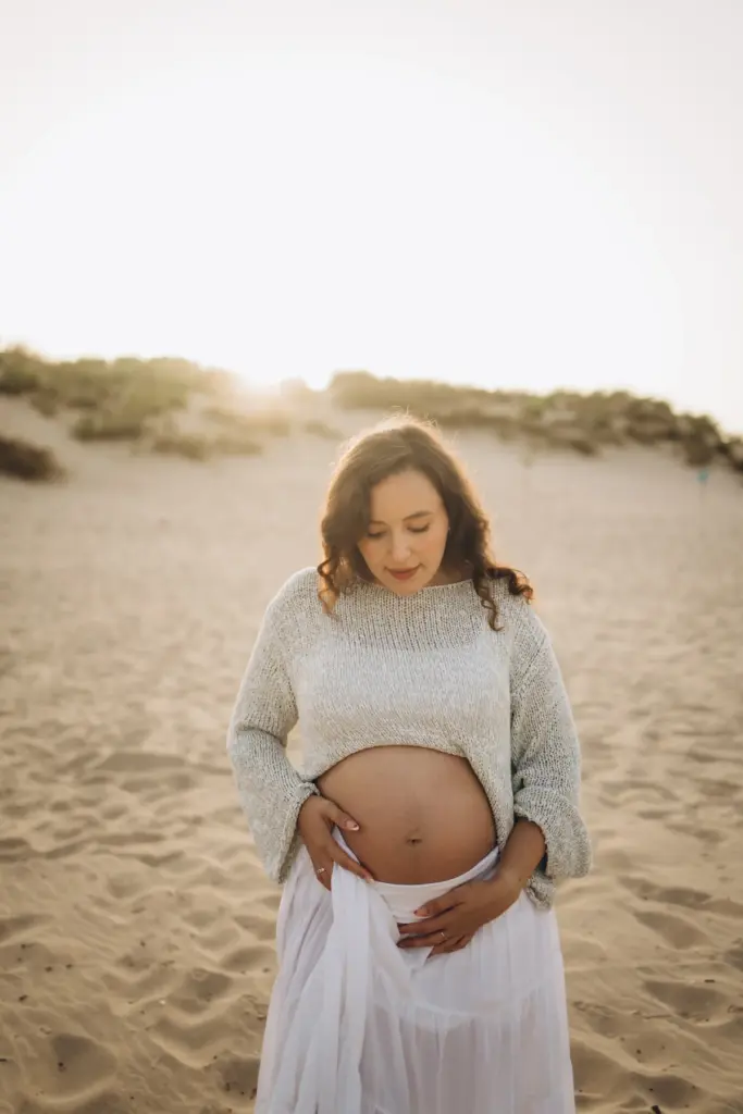 Pregnant woman holding her bump in the dunes at Costa da Caparica